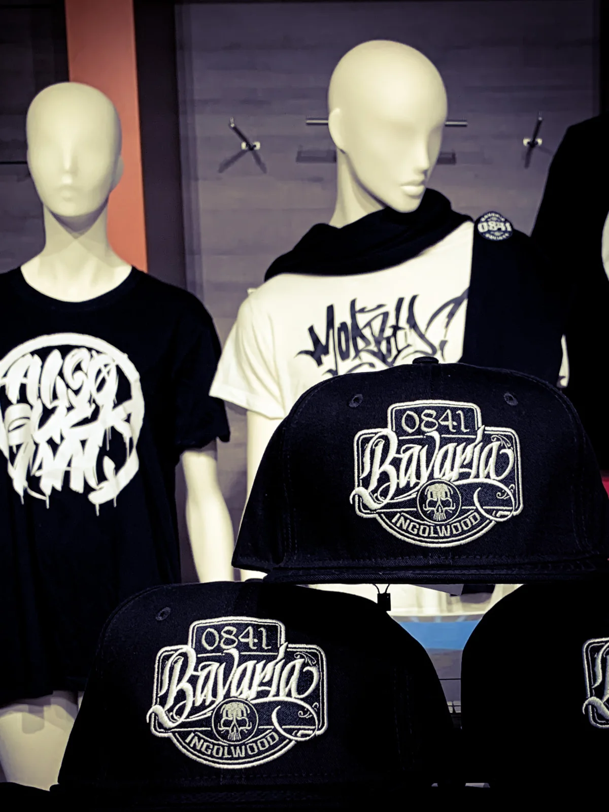 Snapback-Caps mit gesticktem 0841-Bavaria-Ingolwood-Patch im Vordergrund, Shirts auf Puppen dahinter