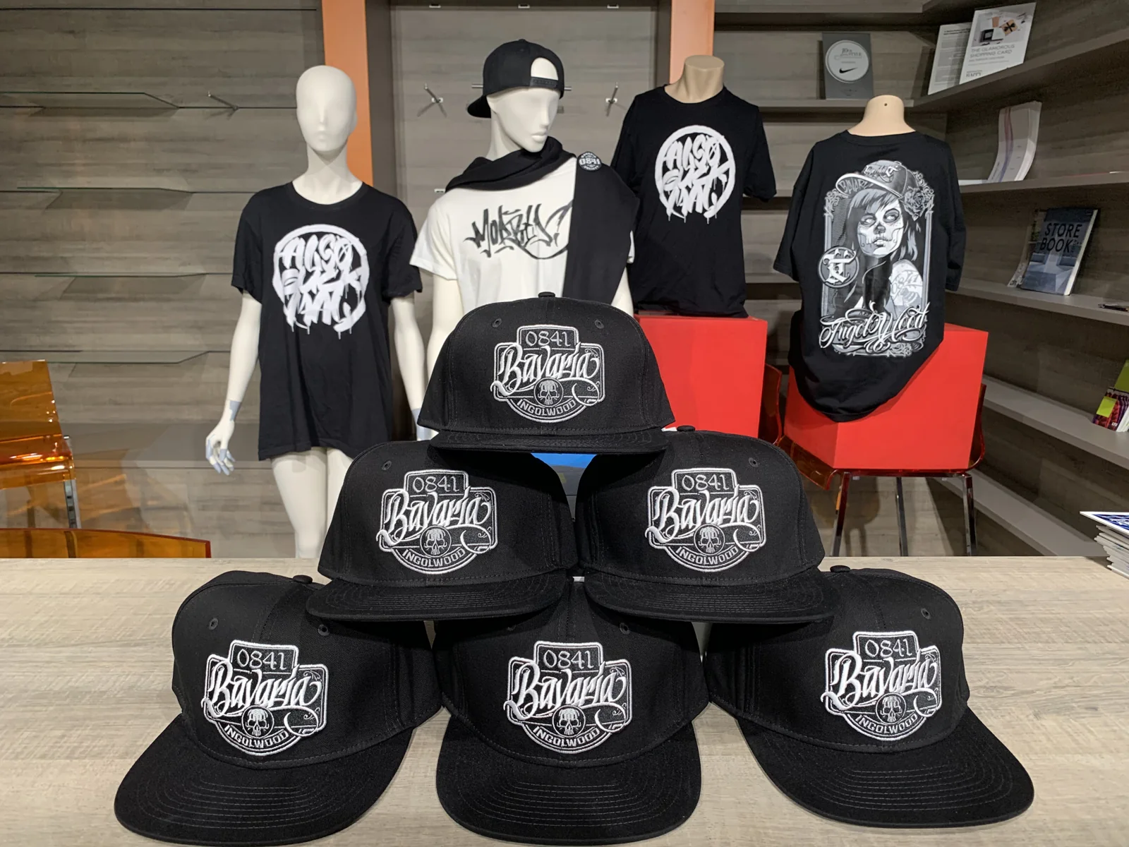 Pyramide aus sechs Snapback-Caps mit Bavaria-Patch, dahinter Shirts auf Puppen