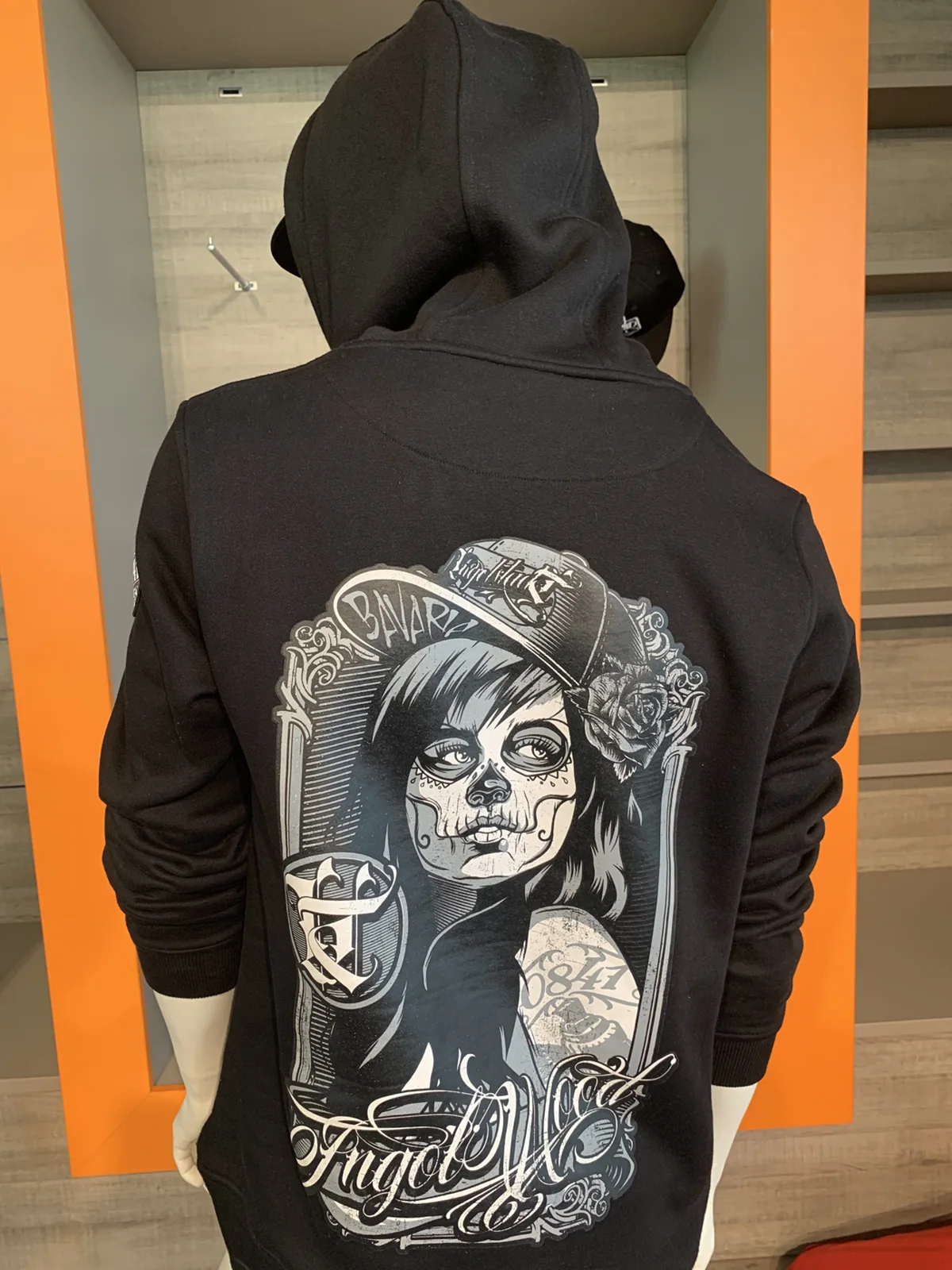 Schwarzer Hoodie von hinten mit Rückenmotiv vor orangefarbener Wand