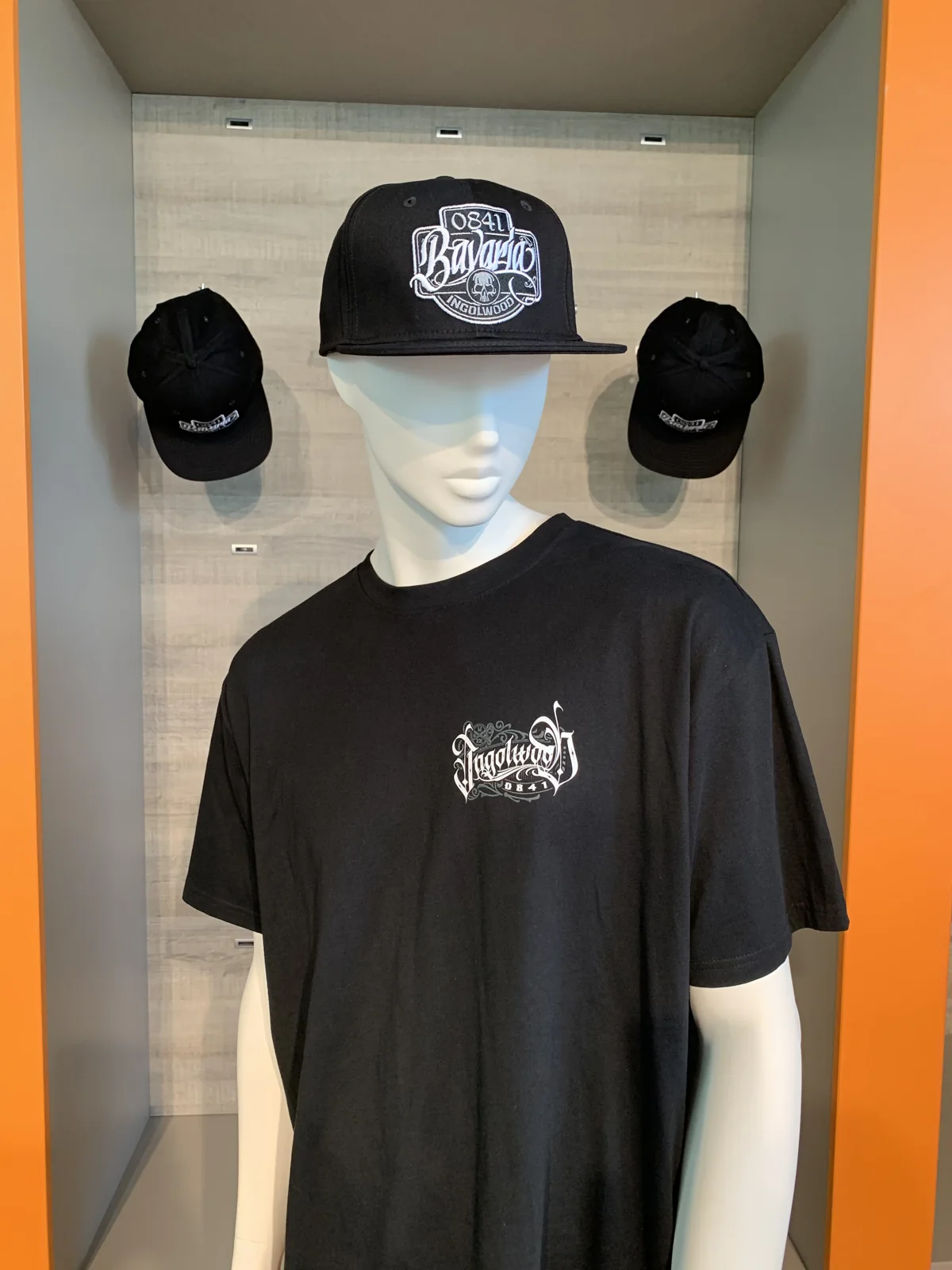 Schwarzes T-Shirt mit Brustlogo und Snapback-Cap auf dem Kopf der Schaufensterpuppe